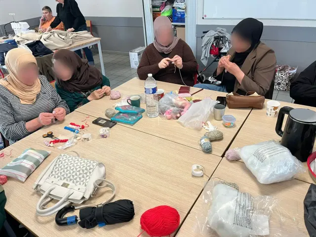 Des participantes tricotent et cousent autour d’une grande table de l’atelier.