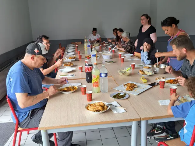 Habitants et animateurs partagent un repas autour d’une grande table.