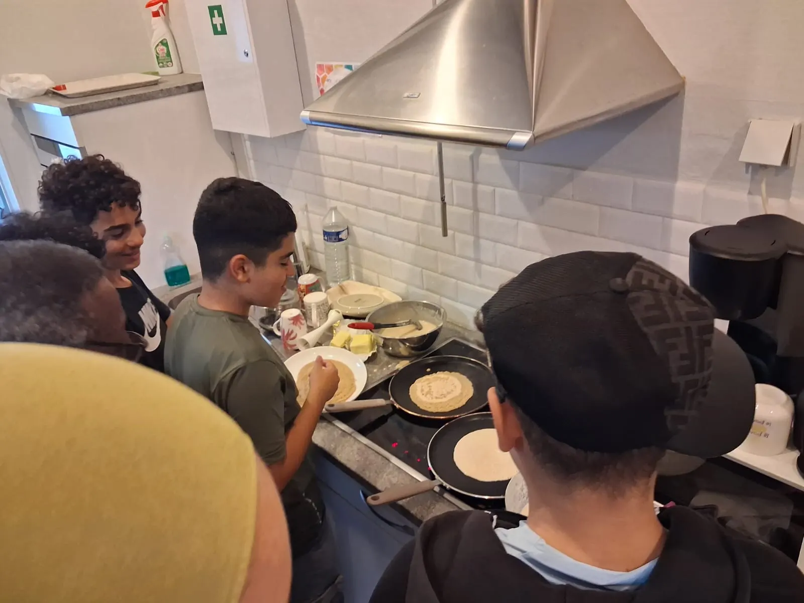 Des adolescents surveillent la cuisson des crêpes sur les plaques de la cuisine