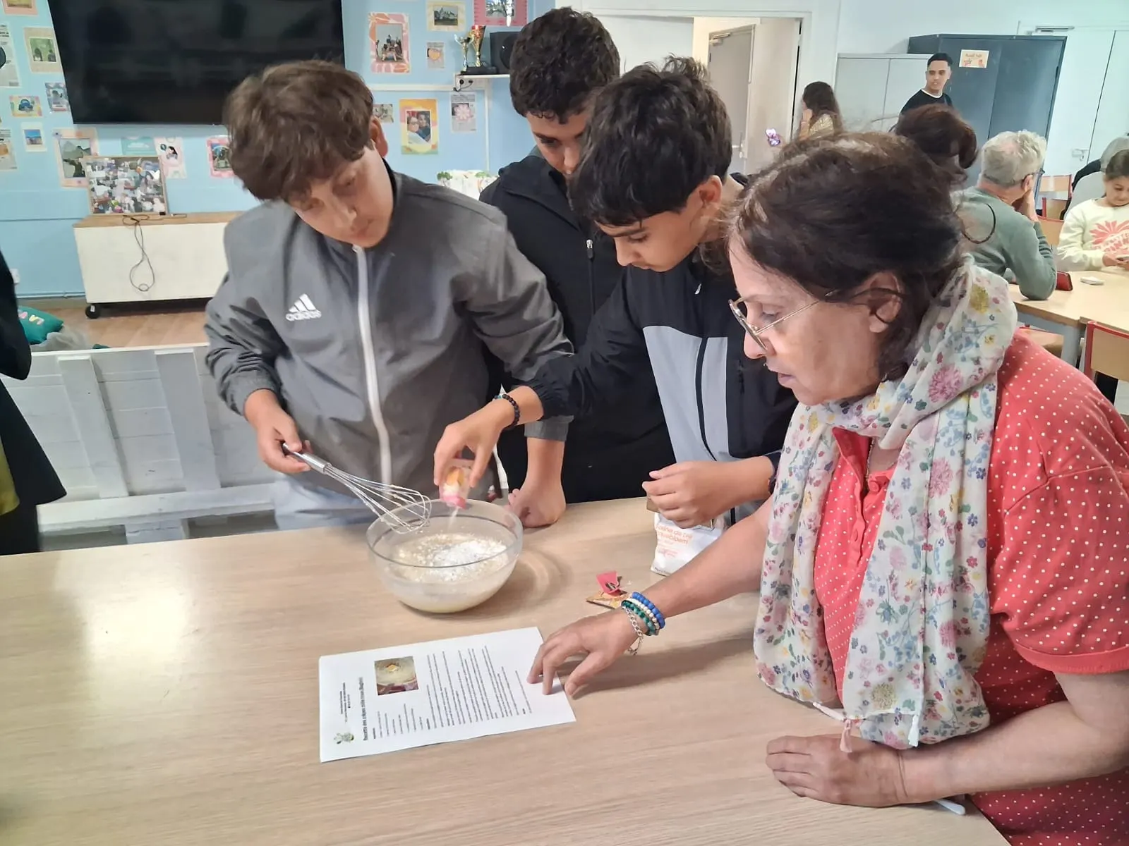 Une senior suit la recette du doigt pendant que trois adolescents ajoutent les ingrédients et fouettent la pâte