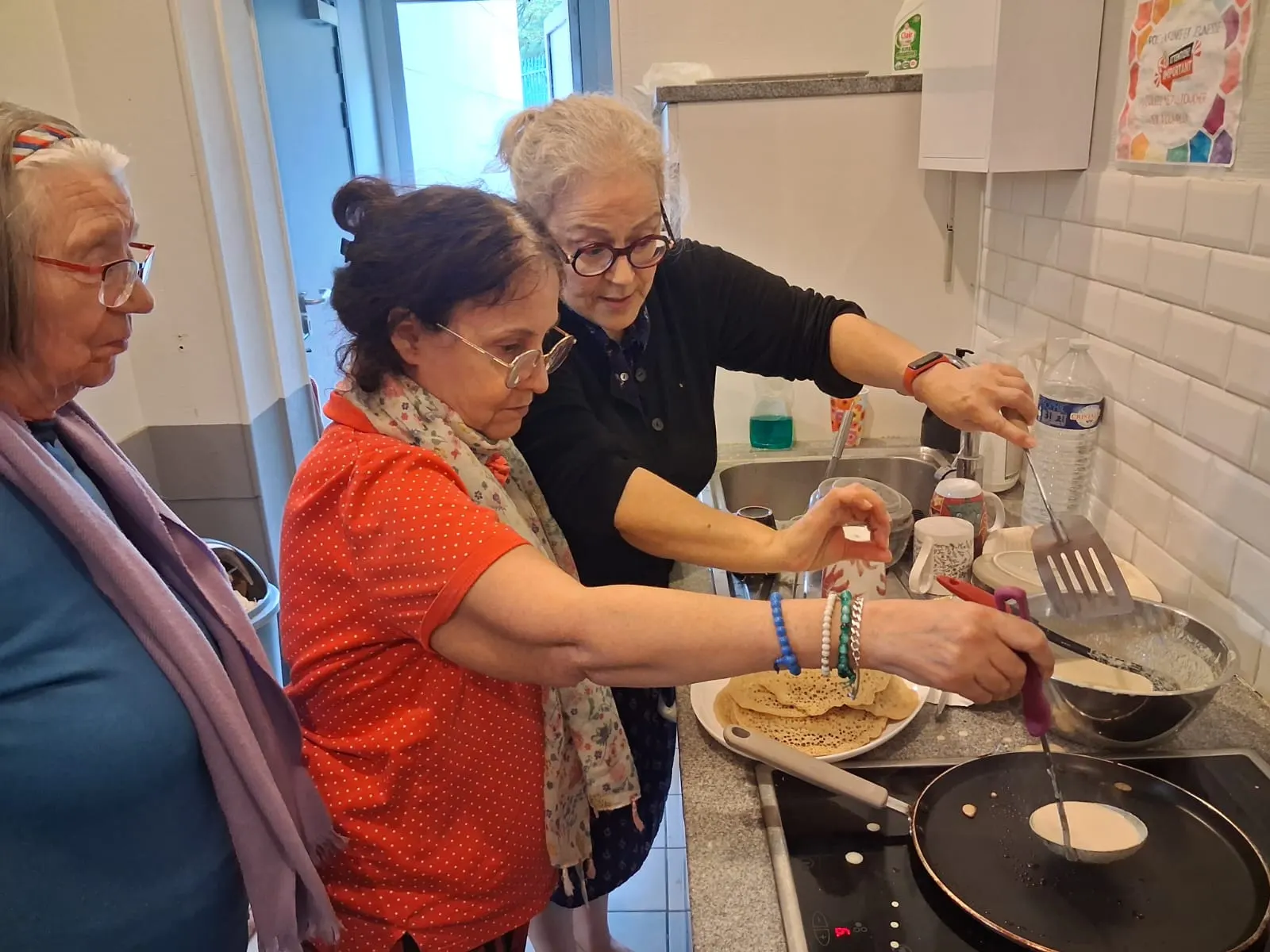 Des seniors font cuire des crêpes à la poêle dans la cuisine du Centre
