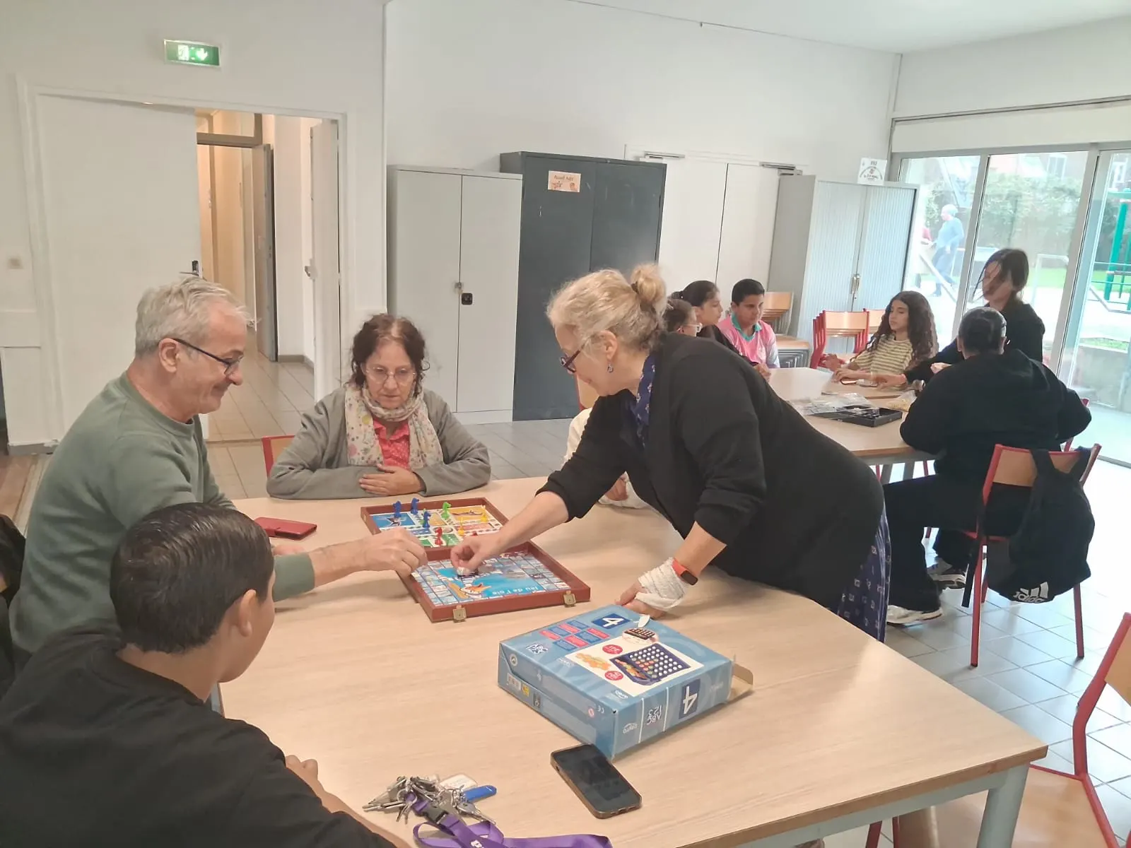 Des seniors et un adolescent jouent aux petits chevaux ; d’autres jeunes jouent à la table voisine