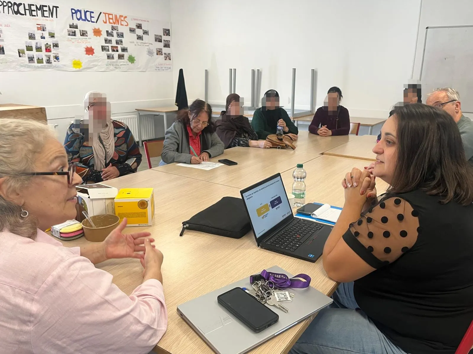 Des participantes autour d’une table écoutent une conseillère installée devant un ordinateur portable