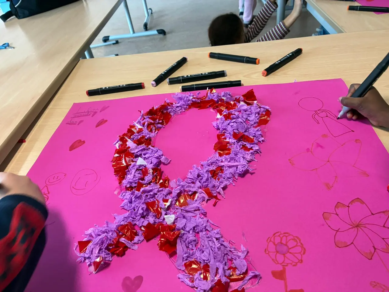 Un grand ruban rose réalisé en papier froissé par les enfants, sur une affiche