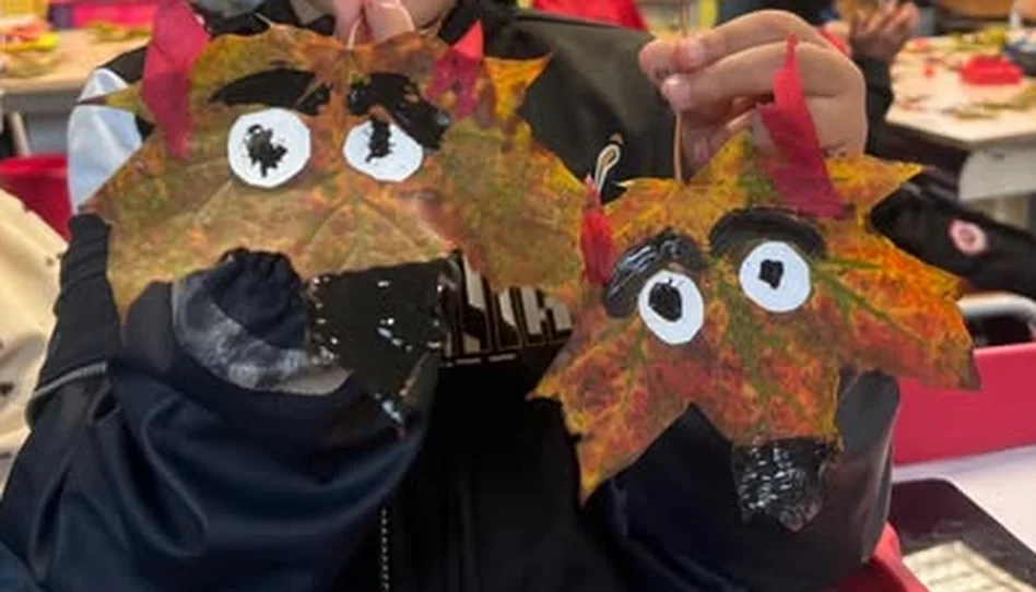 Deux masques réalisés par un enfant avec des feuilles d’automne, des yeux en papier et de la peinture noire