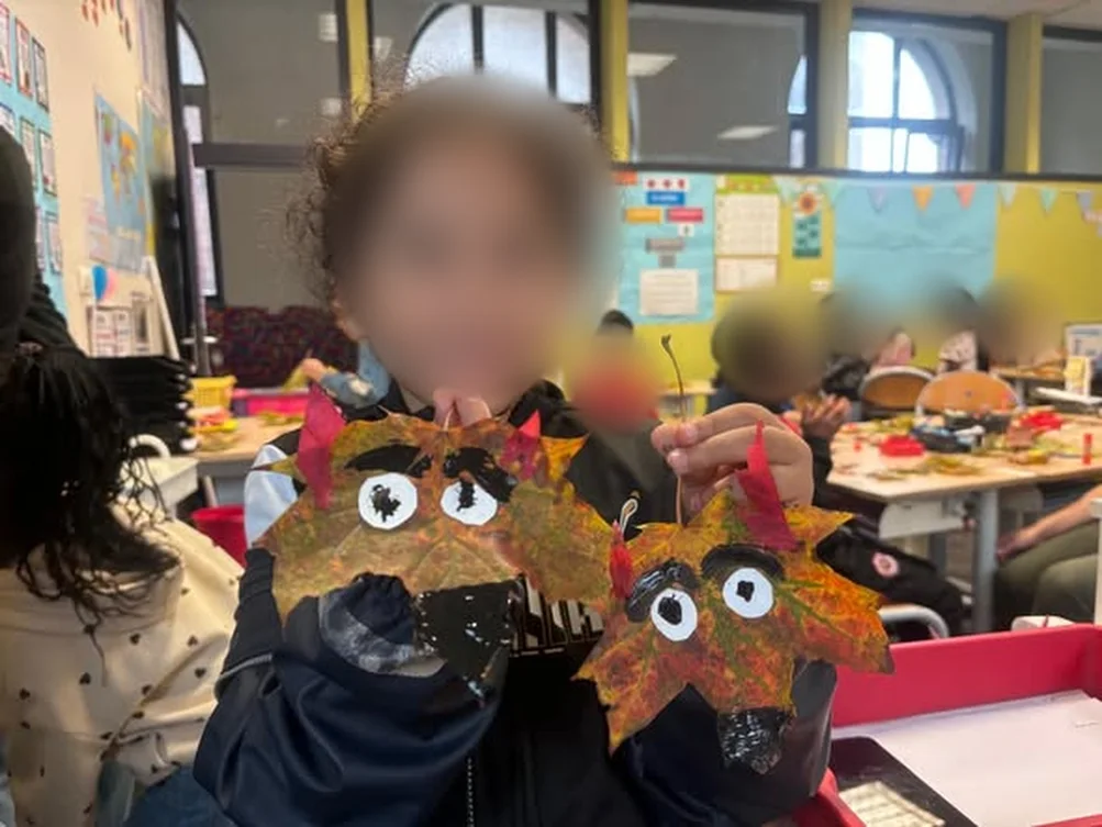 Une enfant montre deux masques réalisés avec des feuilles d’automne (visage flouté)