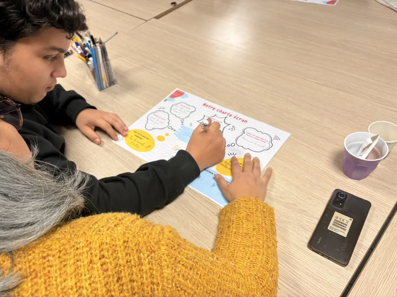 Une mère et son adolescent complètent ensemble une fiche pendant un atelier parentalité