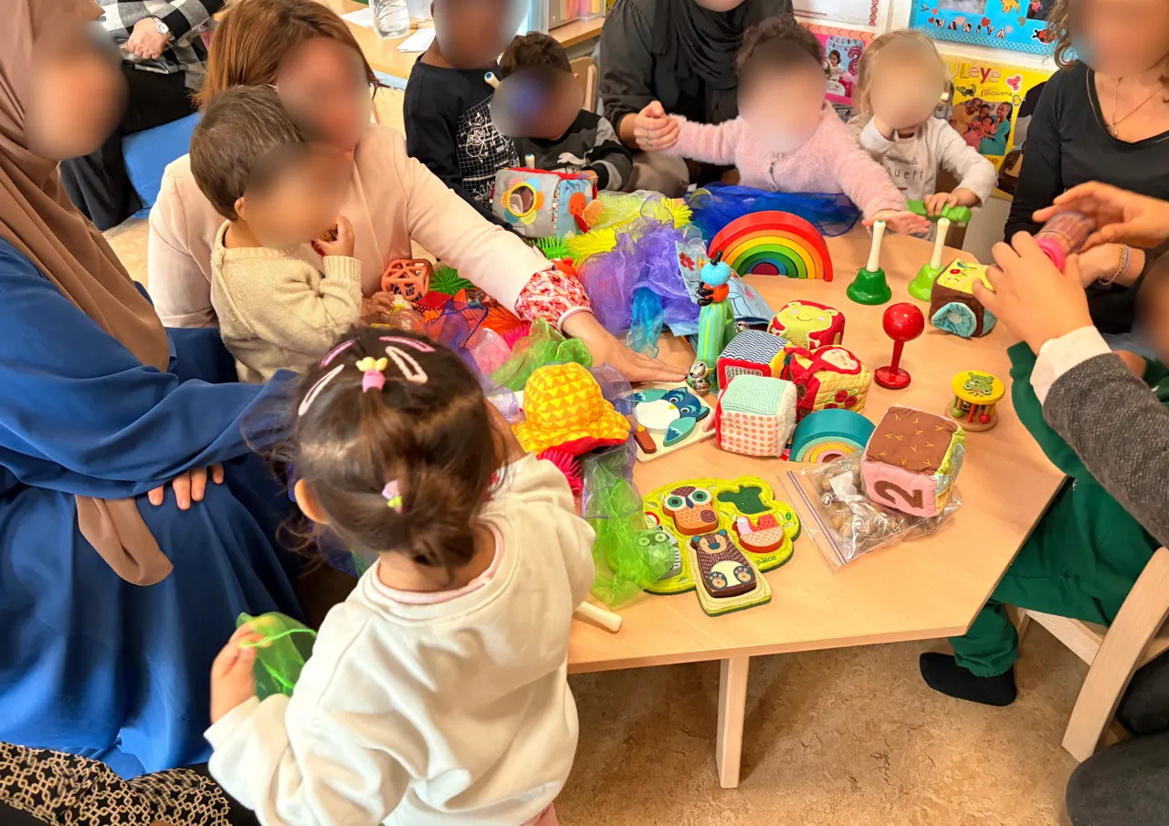 Des parents et leurs tout-petits autour d’une table de jeux d’éveil colorés