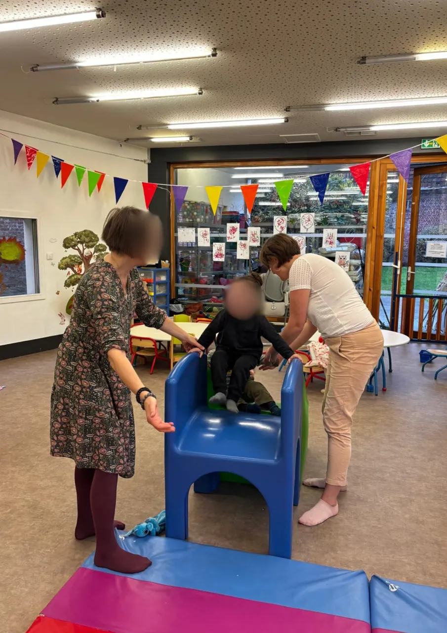 Un tout-petit sur un petit toboggan, accompagné par un parent et une animatrice