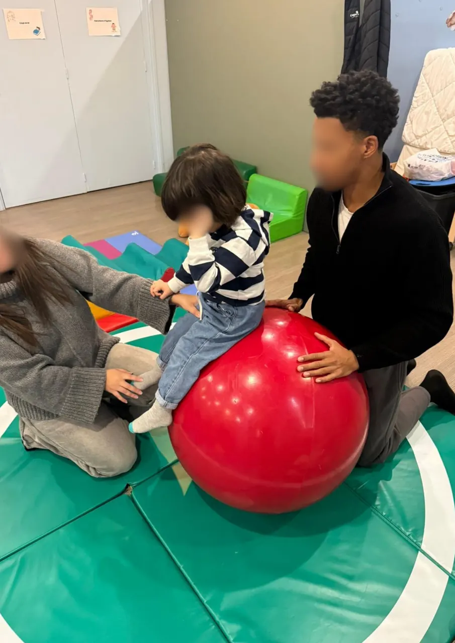 Un parent aide son enfant à tenir en équilibre sur un gros ballon pendant l’atelier motricité