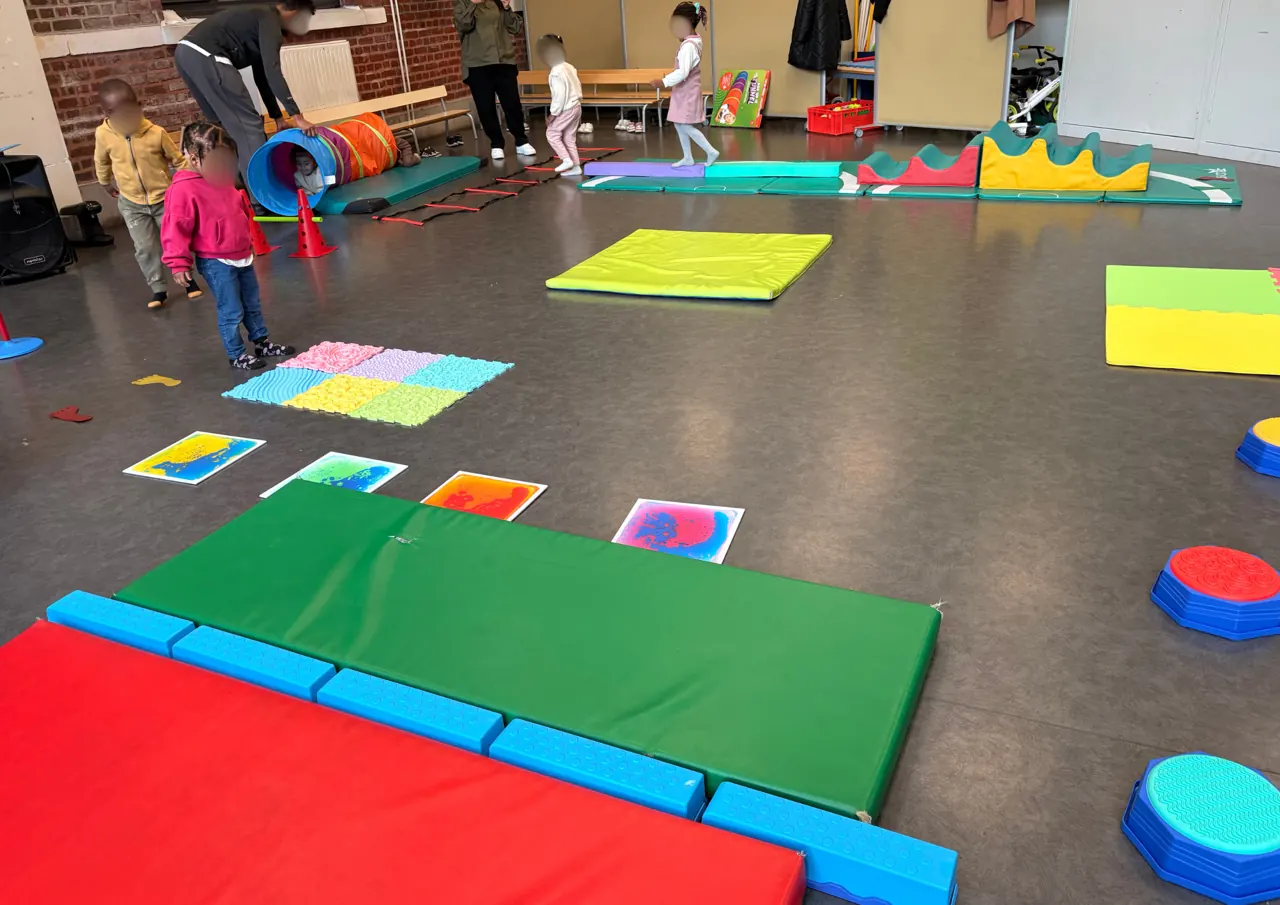 Une salle aménagée avec tapis et modules de motricité pour les enfants et leurs parents